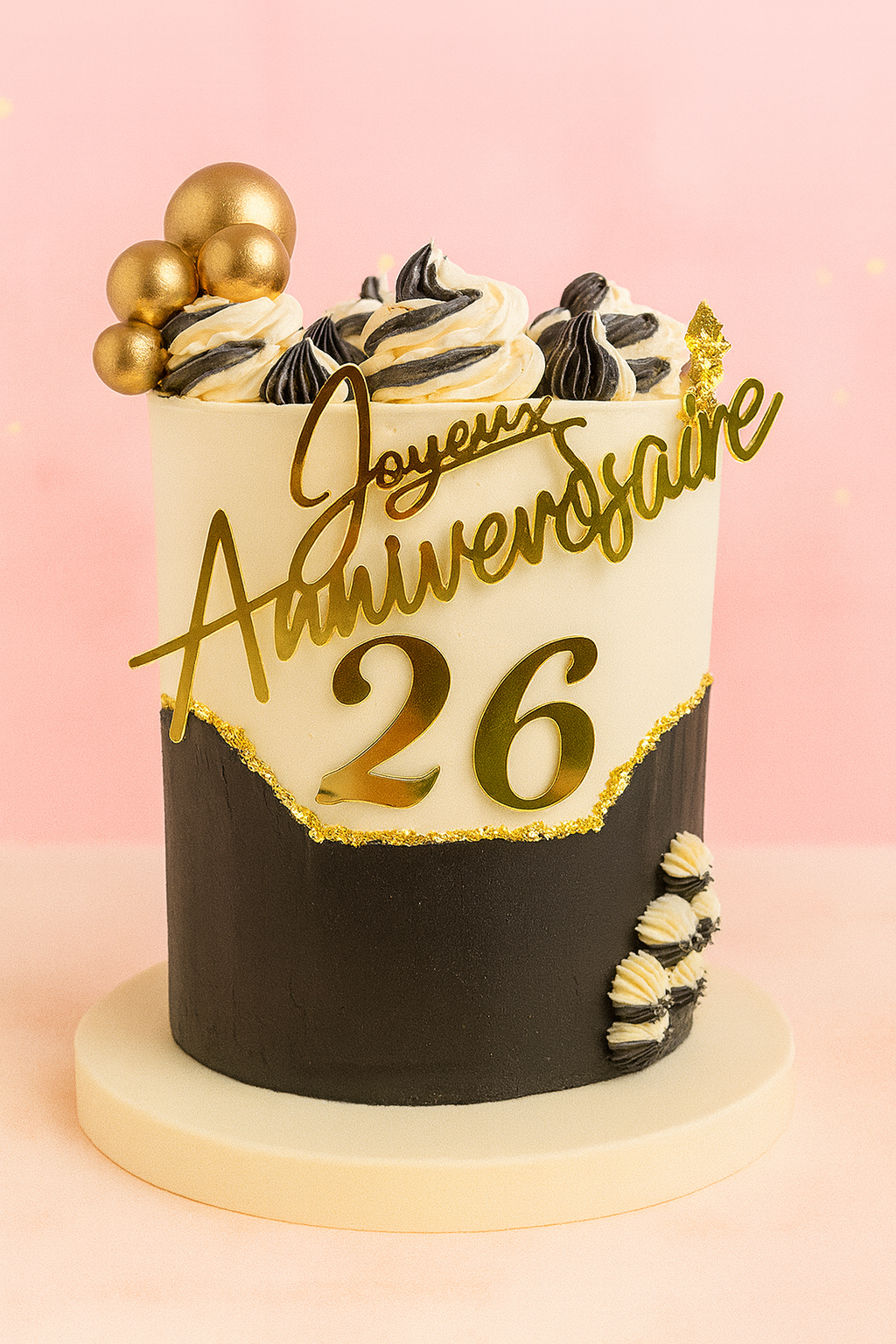Gâteau d’anniversaire noir et or avec feuille d’or, boules dorées, crème bicolore et âge 26 en façade.